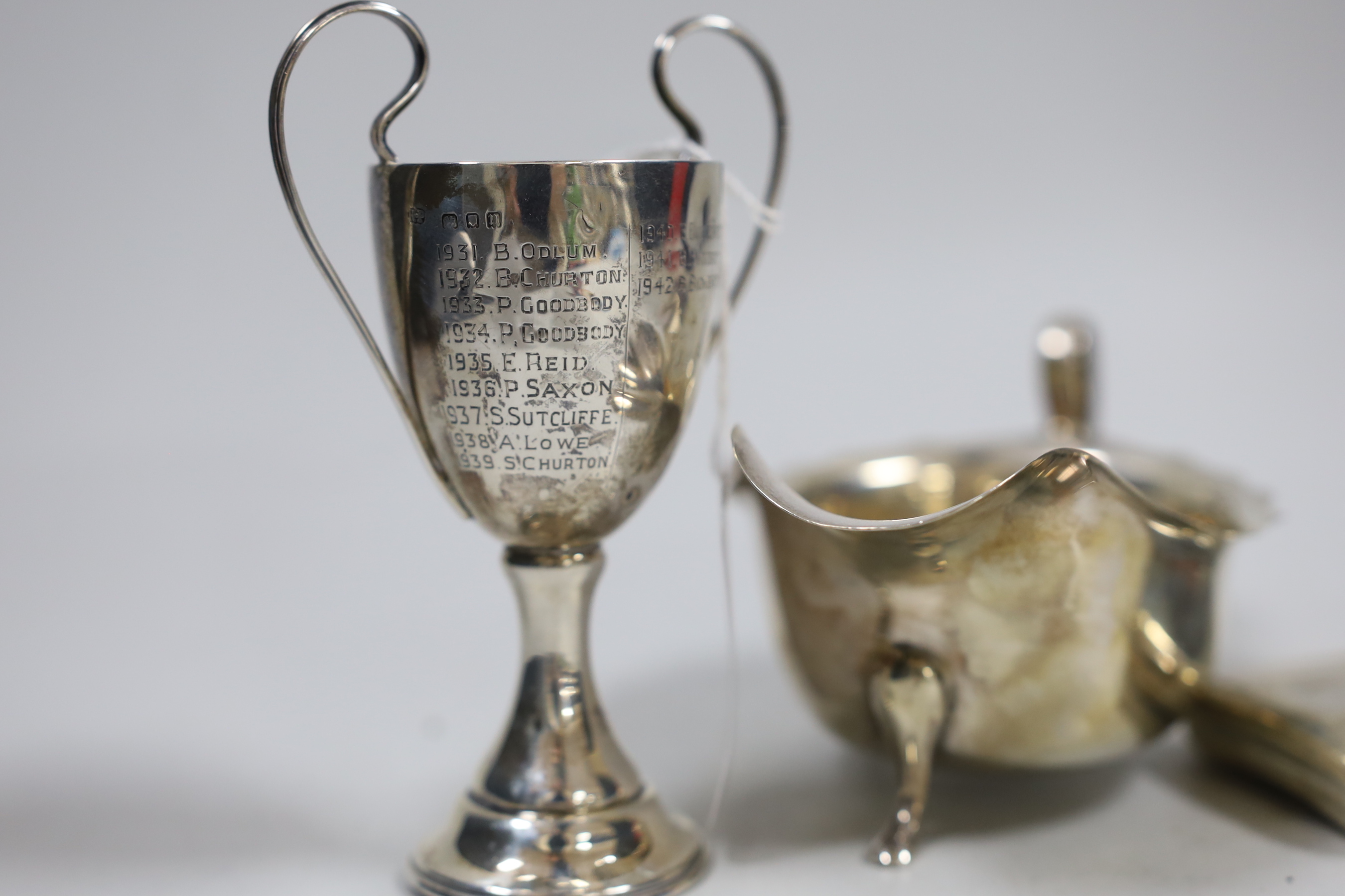 A George V silver sauceboat, a small silver cigarette box, a similar case and a small silver two handled trophy cup.